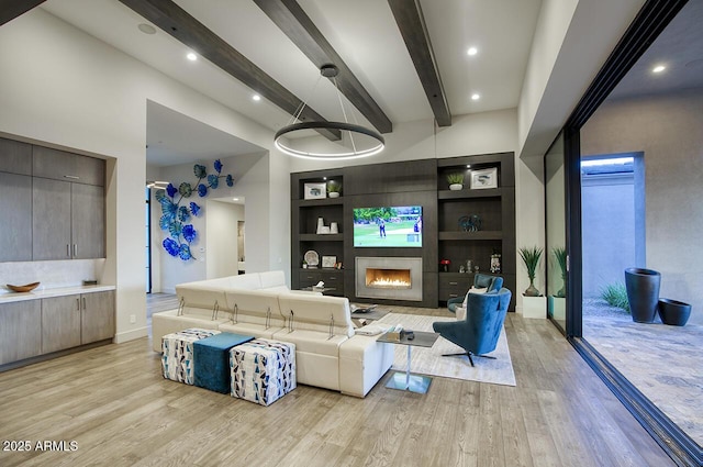 living area with a fireplace, beamed ceiling, light wood-style floors, baseboards, and built in shelves