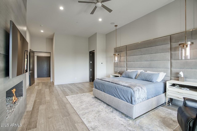bedroom with light wood-style floors, a high ceiling, recessed lighting, and a warm lit fireplace