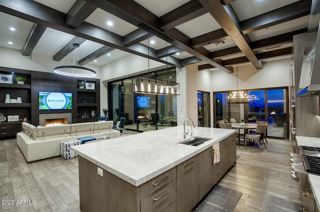 kitchen featuring beam ceiling, a sink, light countertops, light wood finished floors, and a notable chandelier