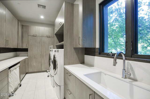 washroom featuring cabinet space, a sink, separate washer and dryer, light tile patterned floors, and visible vents