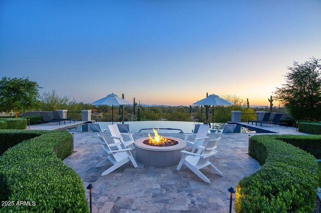 patio terrace at dusk with a fenced in pool and a fire pit