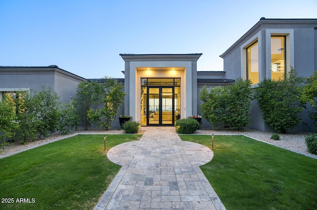 doorway to property with a yard, stucco siding, and french doors