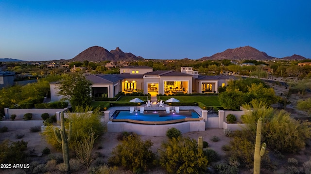 back of property at dusk with fence, an outdoor pool, a mountain view, a patio, and a yard