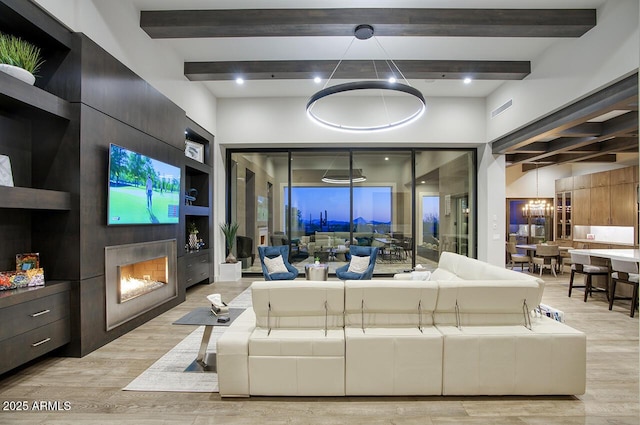 living area with light wood-style floors, a large fireplace, and beamed ceiling