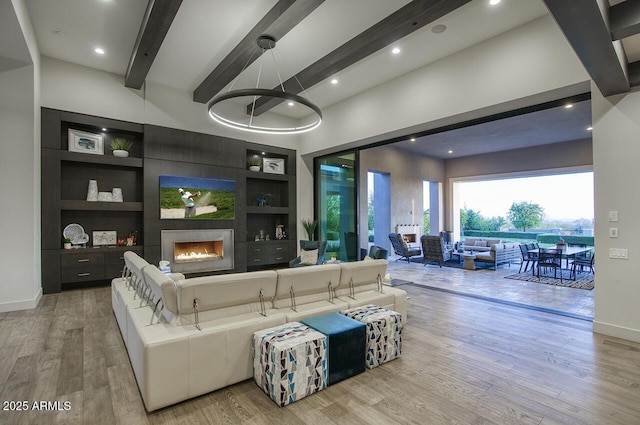 living area with a lit fireplace, built in features, beam ceiling, wood finished floors, and baseboards