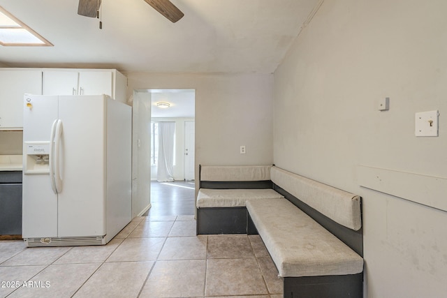 kitchen with light tile patterned floors, a skylight, white refrigerator with ice dispenser, ceiling fan, and white cabinetry