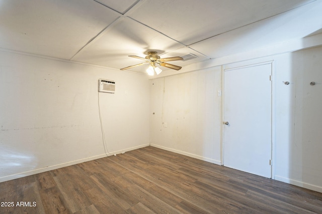 empty room with an AC wall unit, wood finished floors, a ceiling fan, and baseboards