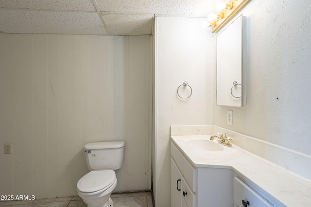 bathroom with a paneled ceiling, tile patterned flooring, toilet, and vanity