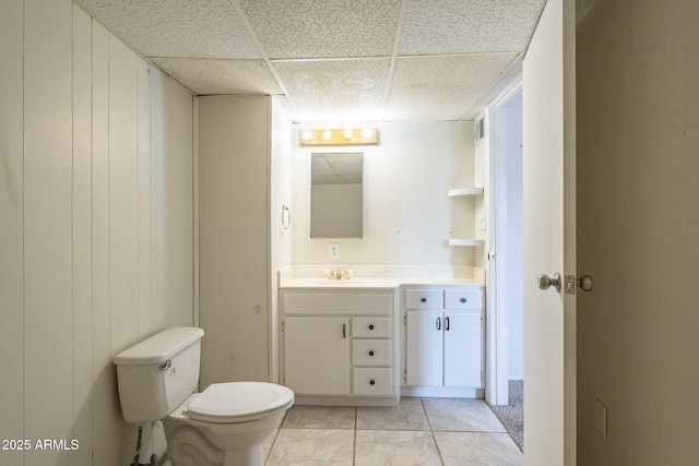 bathroom with tile patterned flooring, toilet, a paneled ceiling, wood walls, and vanity