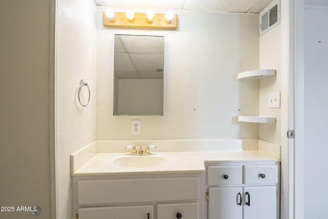 bathroom with a paneled ceiling, vanity, and visible vents