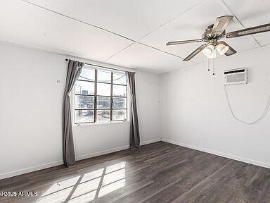 empty room featuring a wall mounted AC, wood finished floors, a ceiling fan, and baseboards