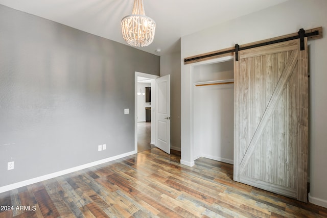 unfurnished bedroom featuring a notable chandelier, wood-type flooring, a barn door, and a closet