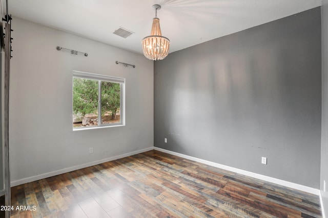 empty room featuring a barn door, hardwood / wood-style flooring, and an inviting chandelier