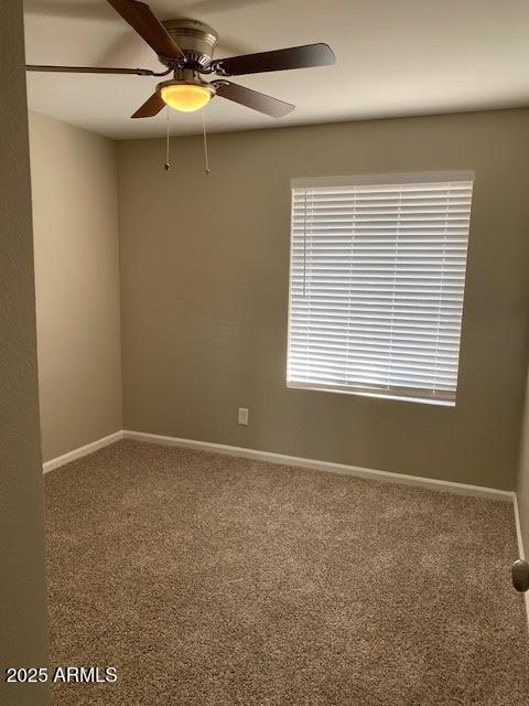 carpeted spare room featuring ceiling fan and baseboards