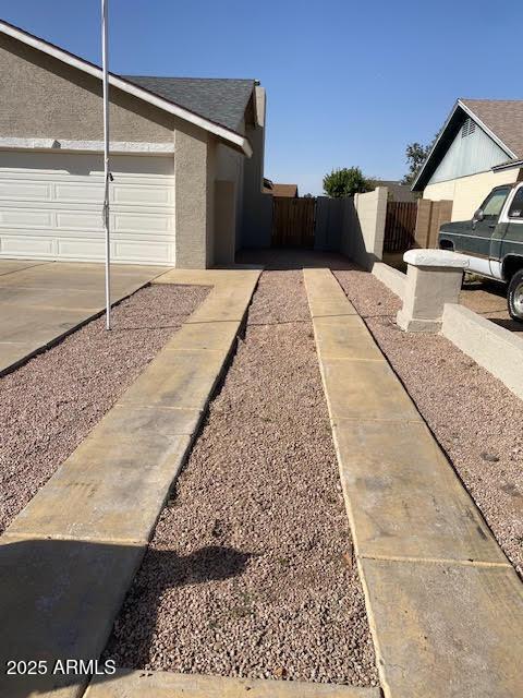 view of side of property featuring stucco siding, an attached garage, and fence