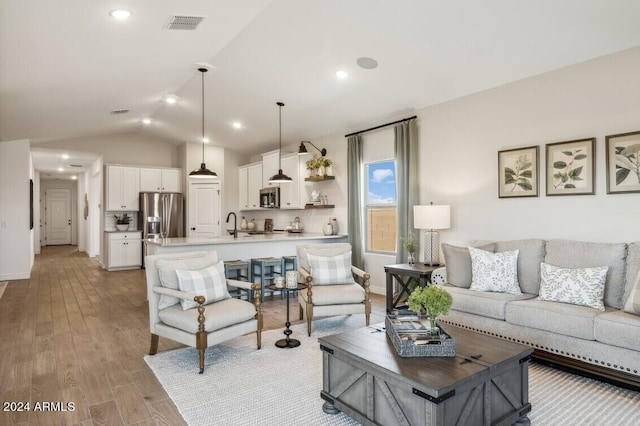 living room with lofted ceiling, sink, and light hardwood / wood-style flooring