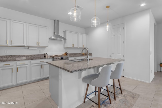 kitchen with pendant lighting, sink, wall chimney exhaust hood, an island with sink, and white cabinetry