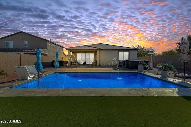 pool at dusk with pool water feature, a patio, and a hot tub