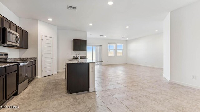 kitchen with visible vents, appliances with stainless steel finishes, light stone countertops, a kitchen island with sink, and a sink