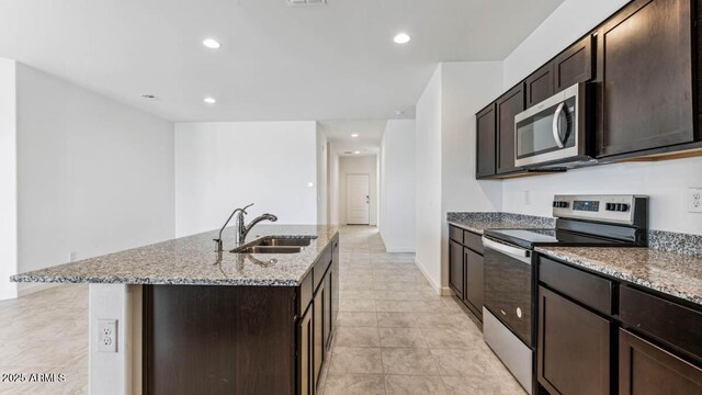 kitchen with dark brown cabinetry, appliances with stainless steel finishes, a kitchen island with sink, a sink, and recessed lighting