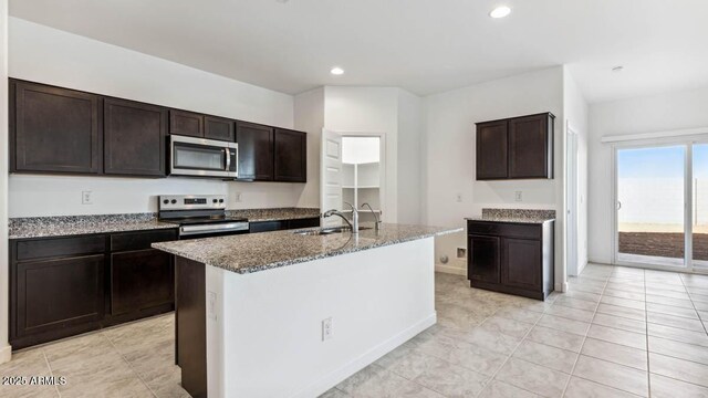 kitchen with a center island with sink, appliances with stainless steel finishes, dark brown cabinets, a sink, and recessed lighting