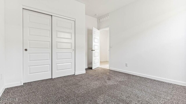 unfurnished bedroom with a closet, dark carpet, and baseboards