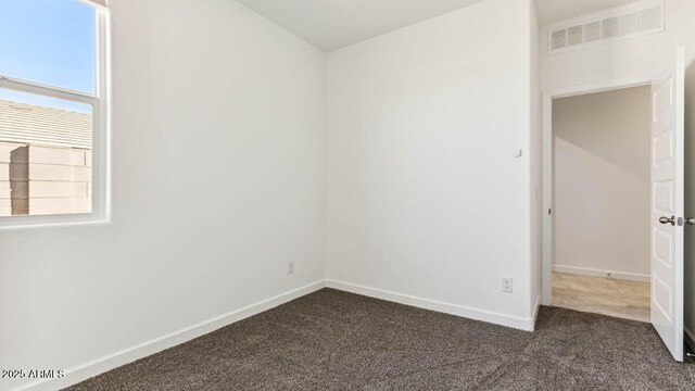 empty room featuring baseboards, visible vents, and dark carpet