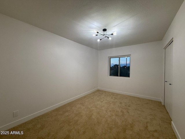empty room featuring light carpet, a chandelier, baseboards, and a textured ceiling