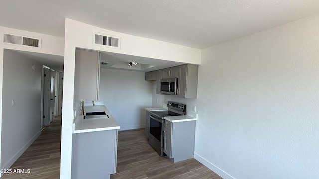 kitchen with appliances with stainless steel finishes, gray cabinetry, a sink, baseboards, and dark wood-style flooring