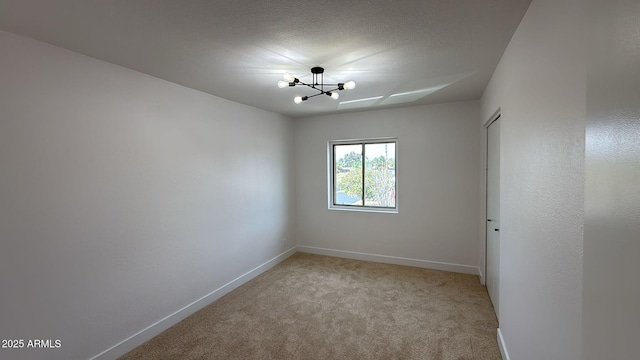 spare room with a chandelier, baseboards, and light colored carpet
