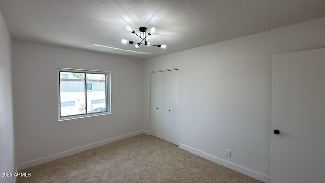 unfurnished room featuring a chandelier, light carpet, baseboards, and a textured ceiling