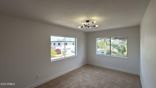 unfurnished room featuring a chandelier, light colored carpet, and baseboards