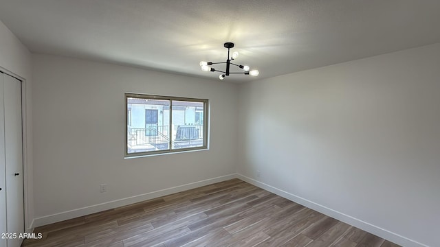 unfurnished room featuring a chandelier, wood finished floors, and baseboards