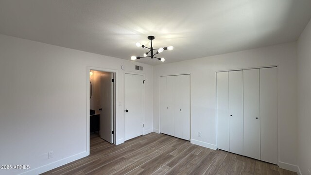 unfurnished bedroom with a chandelier, two closets, wood finished floors, and baseboards
