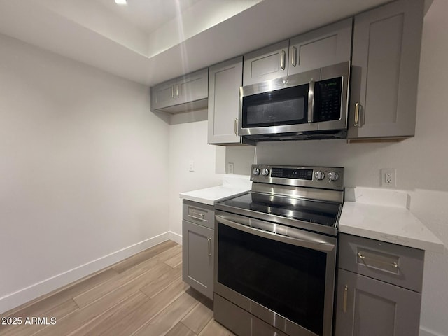 kitchen with stainless steel appliances, gray cabinetry, light wood-style floors, baseboards, and a tray ceiling