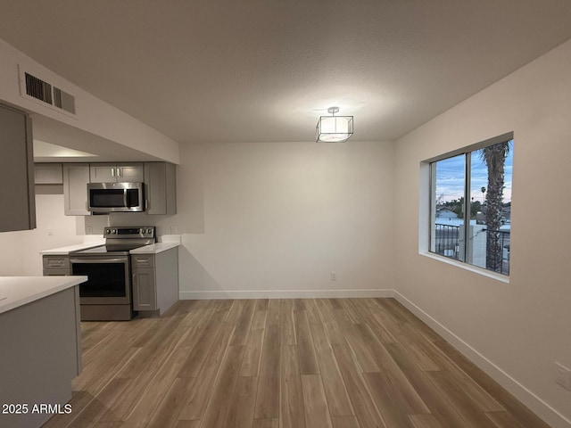 kitchen featuring appliances with stainless steel finishes, gray cabinets, light wood-type flooring, and light countertops