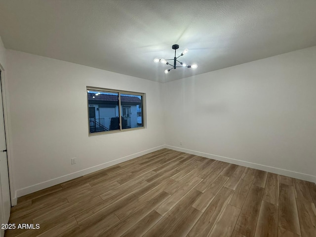 unfurnished room featuring wood finished floors, a chandelier, and baseboards