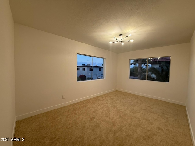empty room with a chandelier, carpet floors, and baseboards