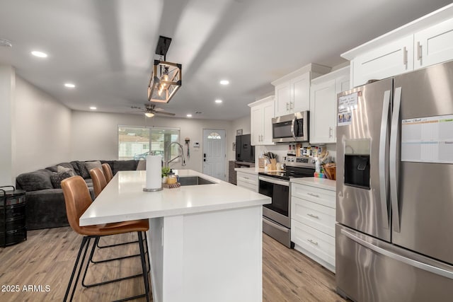 kitchen featuring a kitchen bar, light wood-style flooring, a sink, open floor plan, and stainless steel appliances