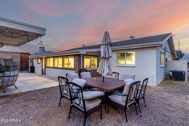 back of property at dusk with outdoor dining area, brick siding, central AC unit, and a patio area