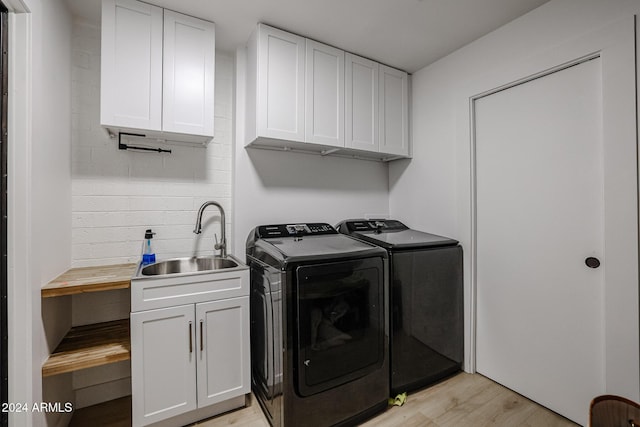 washroom featuring washer and dryer, sink, cabinets, and light wood-type flooring