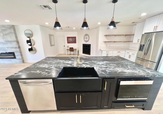 kitchen with pendant lighting, a large island with sink, a fireplace, white cabinetry, and stainless steel appliances