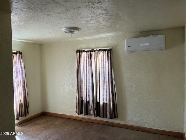 empty room with an AC wall unit, a textured wall, a textured ceiling, and wood finished floors