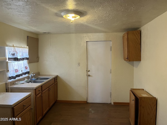 kitchen featuring a textured wall, a sink, a textured ceiling, wood finished floors, and baseboards