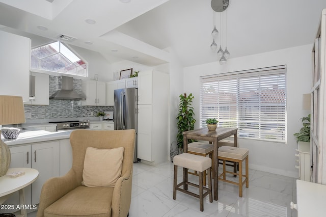 kitchen featuring wall chimney range hood, white cabinetry, hanging light fixtures, stainless steel appliances, and tasteful backsplash