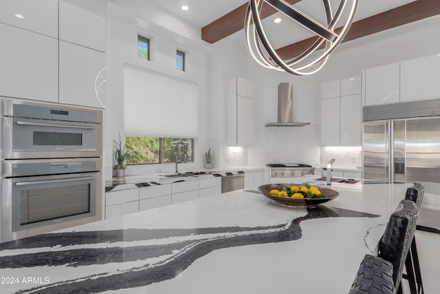 kitchen featuring white cabinets, dark stone countertops, beamed ceiling, and wall chimney range hood