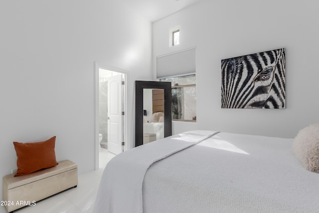 bedroom with ensuite bathroom, light tile patterned flooring, and a towering ceiling