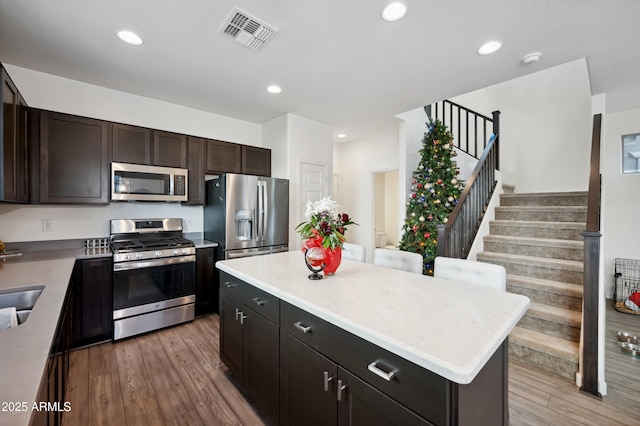 kitchen featuring a kitchen island, wood-type flooring, appliances with stainless steel finishes, and dark brown cabinetry