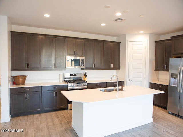 kitchen featuring sink, dark brown cabinets, a center island with sink, light wood-type flooring, and stainless steel appliances