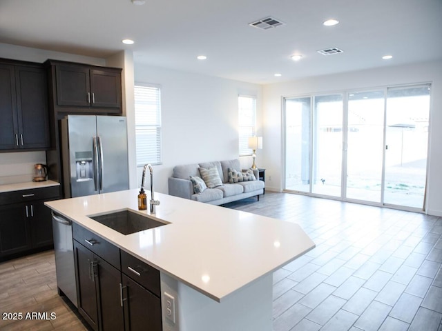 kitchen with an island with sink, appliances with stainless steel finishes, sink, and light wood-type flooring